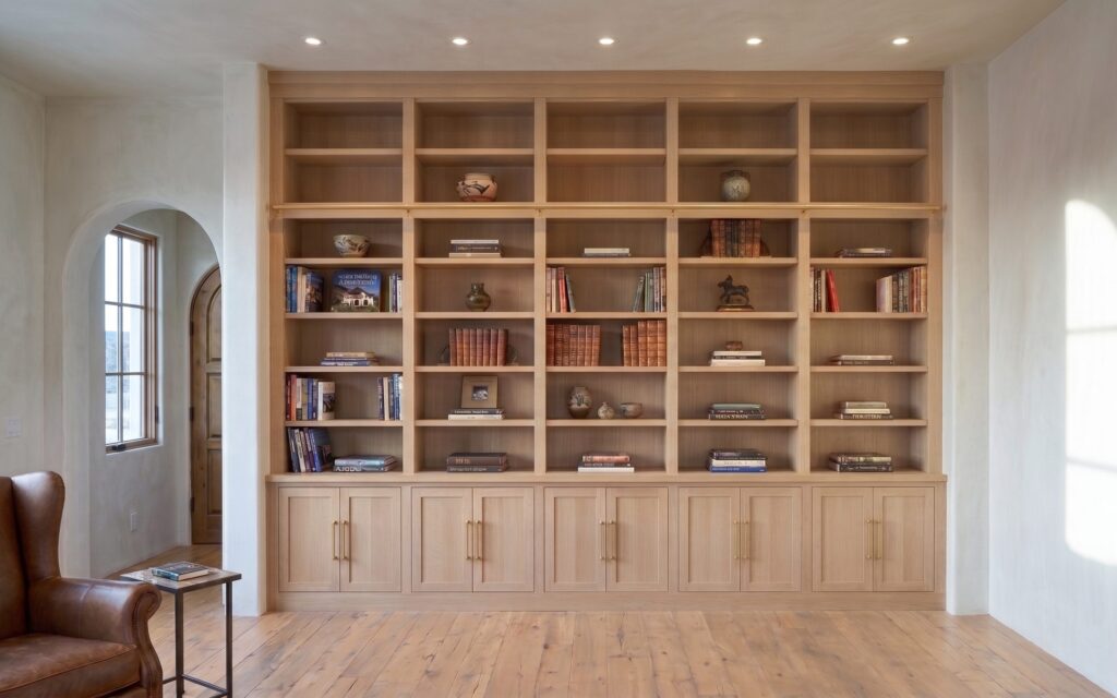 A light wood built-in bookcase wall with open shelves above and Shaker doors with brass pulls below.