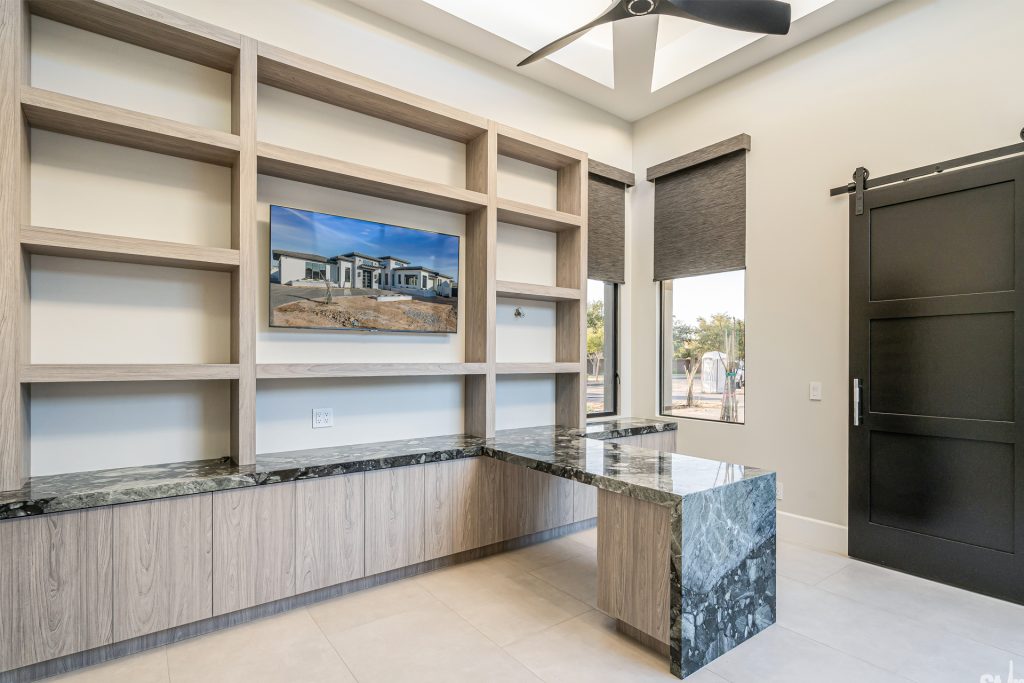 Modern office desk with a marble top and wooden shelving unit, featuring a wall-mounted screen above the desk.