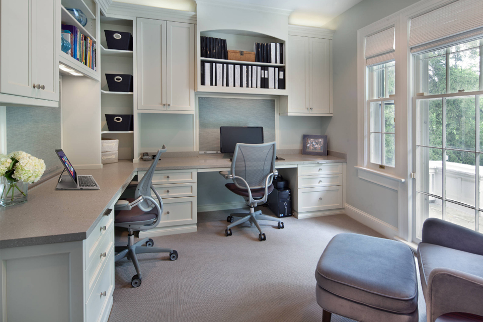Transitional shaker-style white cabinets with stone quartz countertops in a home office setup featuring a desk and ergonomic chairs.