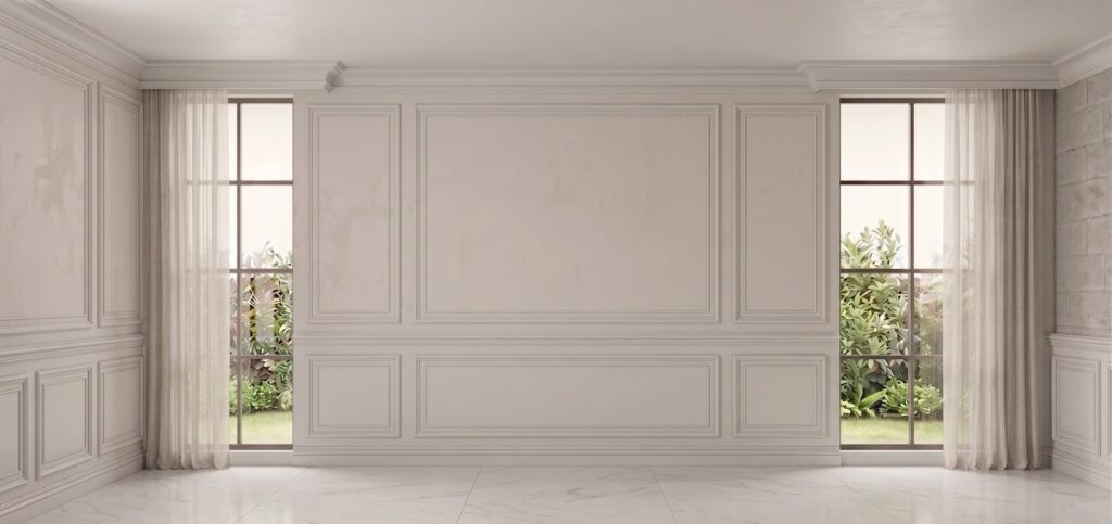 An empty room with warm white picture-frame panels, crown molding, two tall windows and a marble-look floor.